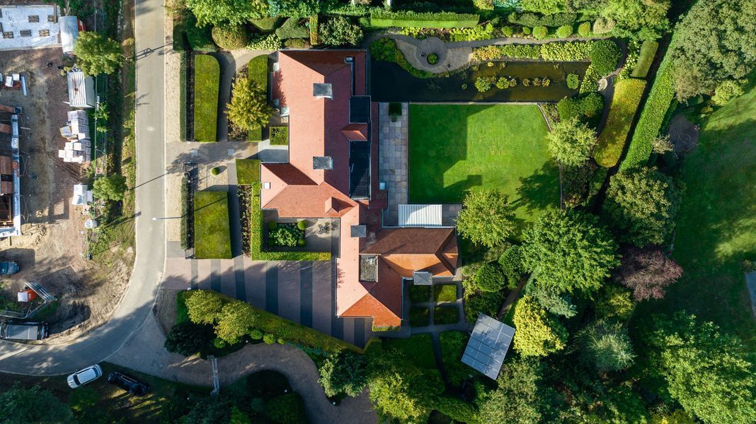 Luchtfoto van een huis met een rood dak en een binnenplaats, omgeven door bomen en tuinen.