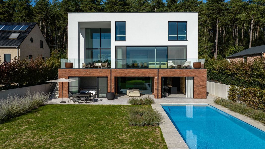 Moderne witte woning met twee verdiepingen, grote ramen, houten terras en zwembad in de achtertuin.