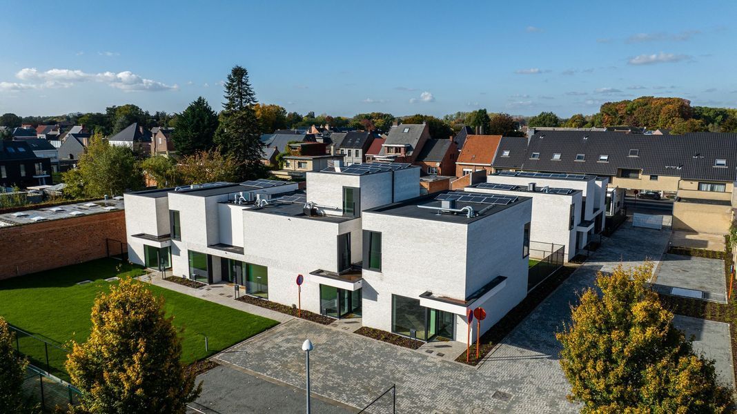 Moderne, witte rijtjeshuizen met platte daken in een zonnige woonwijk, gezien van bovenaf.