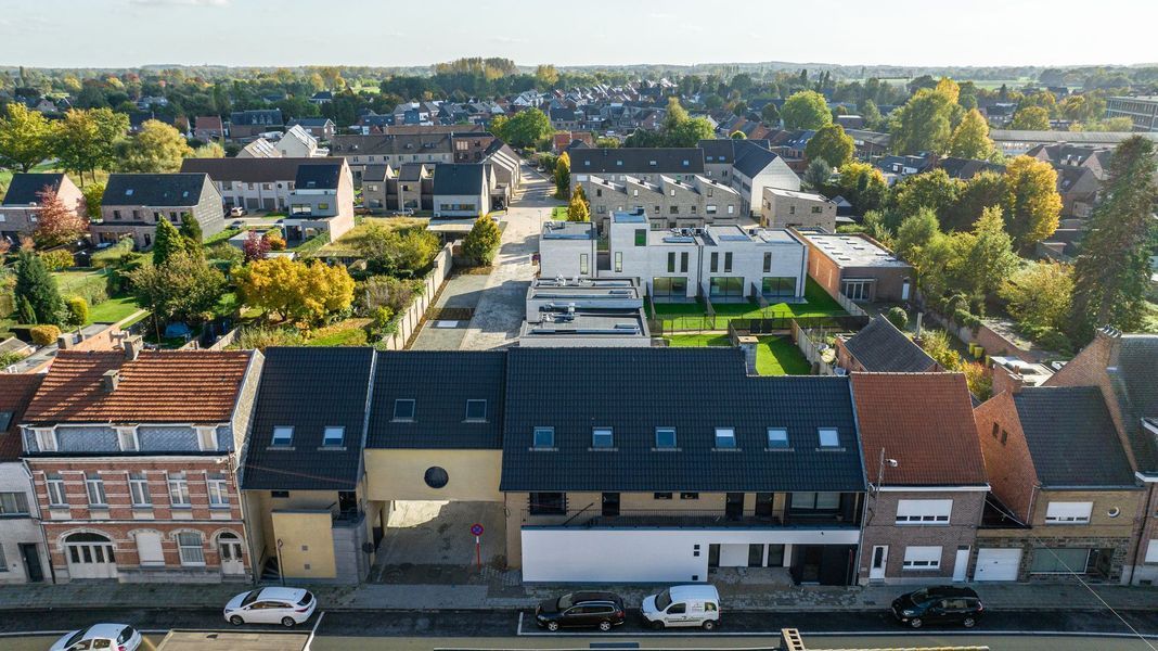 Luchtfoto van een stadsplein met historische gebouwen, bomen en daken bij helder daglicht.
