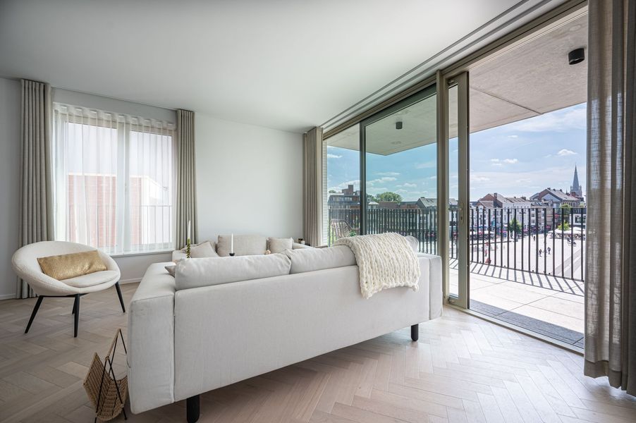 Moderne woonkamer met witte bank, fauteuil en glazen schuifdeuren met uitzicht op de stad.