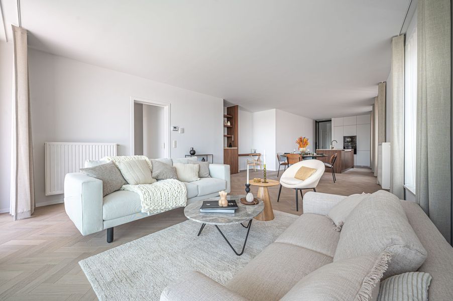 Lichte, moderne woonkamer met crèmekleurige banken, salontafel en grote ramen.