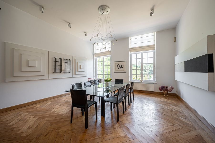 Lichte, moderne eetkamer met een glazen tafel, zwarte stoelen, witte muren, grote ramen en houten vloeren.