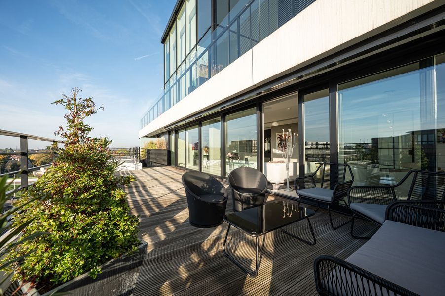 Modern balkon met zitgelegenheid buiten en uitzicht over de stad, grenzend aan een gebouw met glazen wanden.