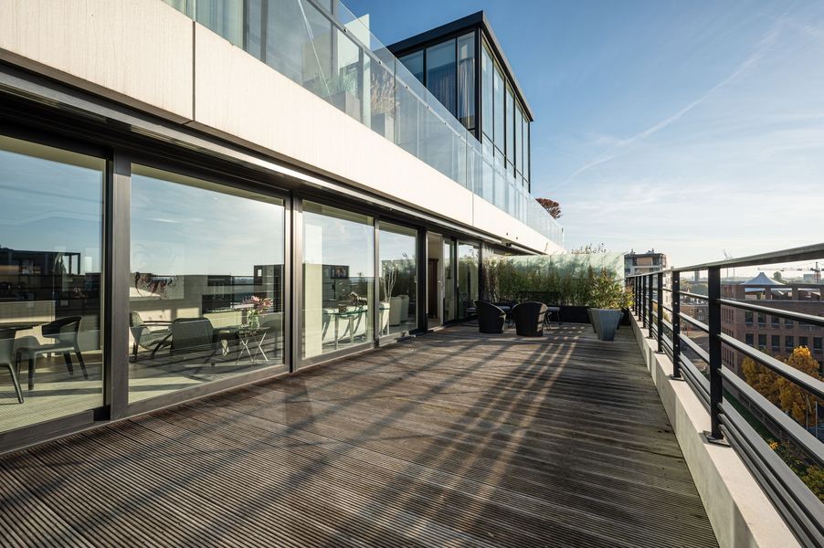 Dakterras met glazen wanden, metalen vloer en moderne zitgelegenheid naast een gebouw