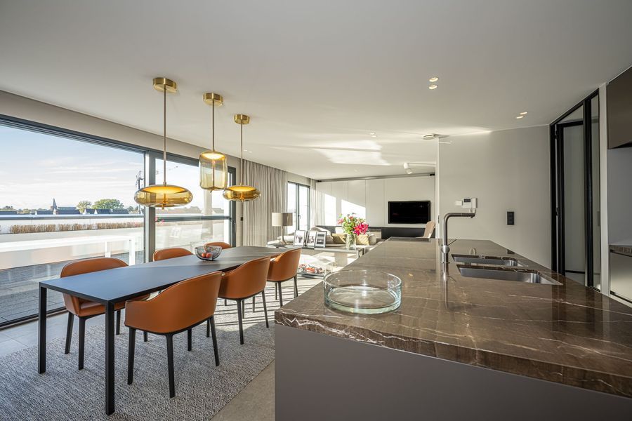 Moderne open eet- en keukenruimte met hanglampen, barzitjes en uitzicht op het water.