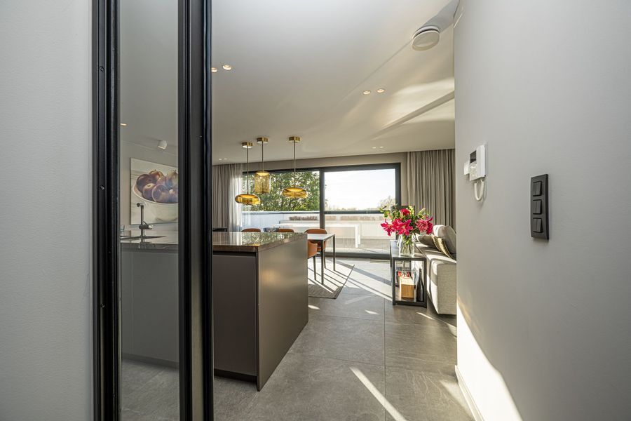 Moderne open keuken en eetruimte met veel daglicht, glazen deuren en een vaas met roze bloemen.