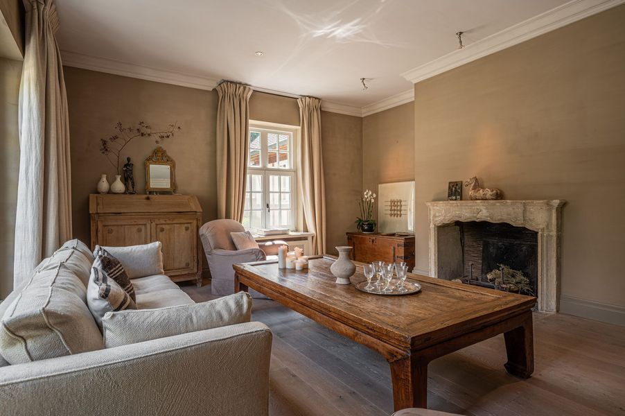 Gezellige beige woonkamer met een grote houten salontafel, open haard en raam met gordijnen.