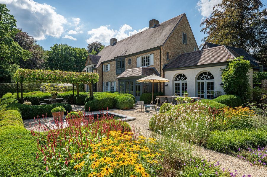 Stenen huis met een tuin, parasols en kleurrijke bloemen onder een helderblauwe hemel.