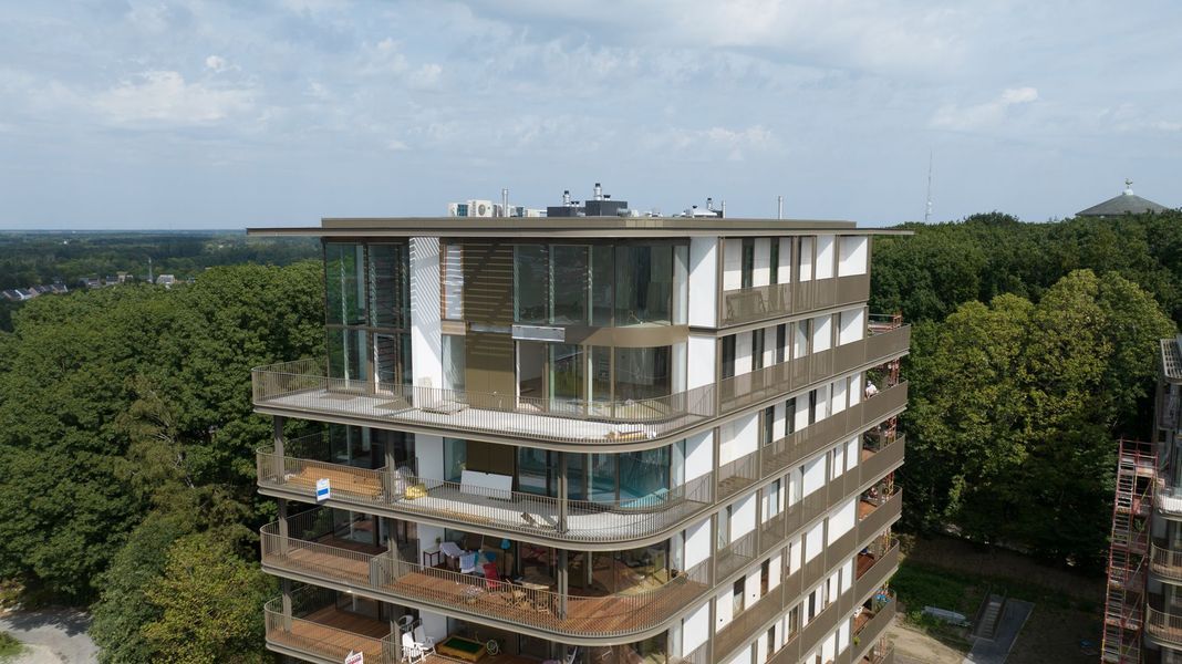 Modern, meerlaags glazen kantoorgebouw, omgeven door weelderige groene bomen, gezien vanaf boven.