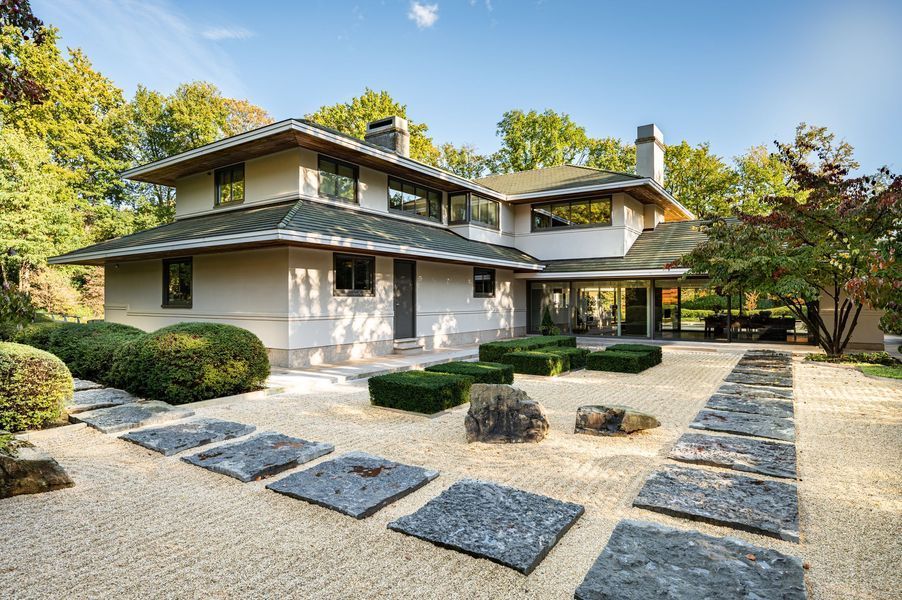 Moderne woning met twee verdiepingen, een stenen pad, een grindtuin en keurig gesnoeide struiken onder een heldere hemel.