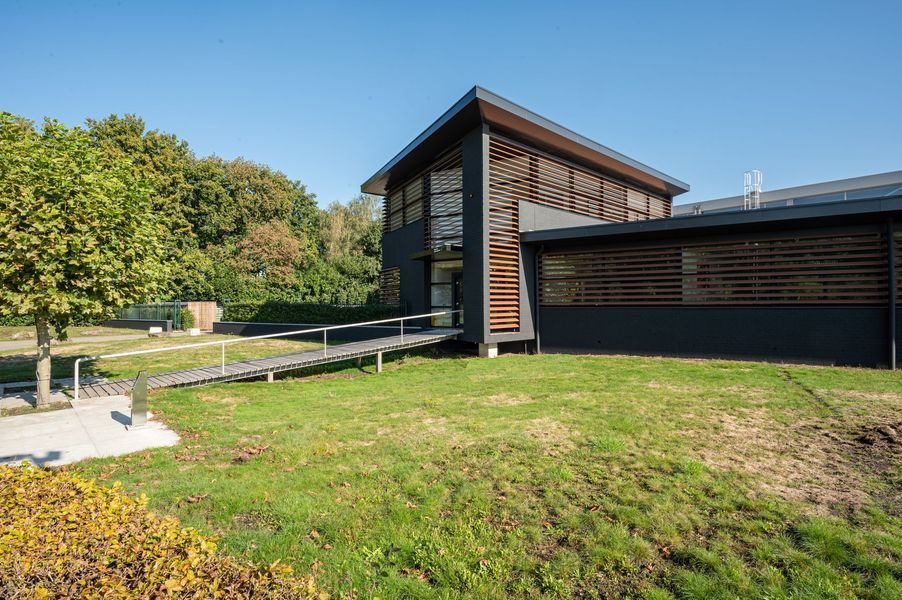 Modern gebouw met houten gevelbekleding naast een grasveld en bomen, onder helder daglicht.