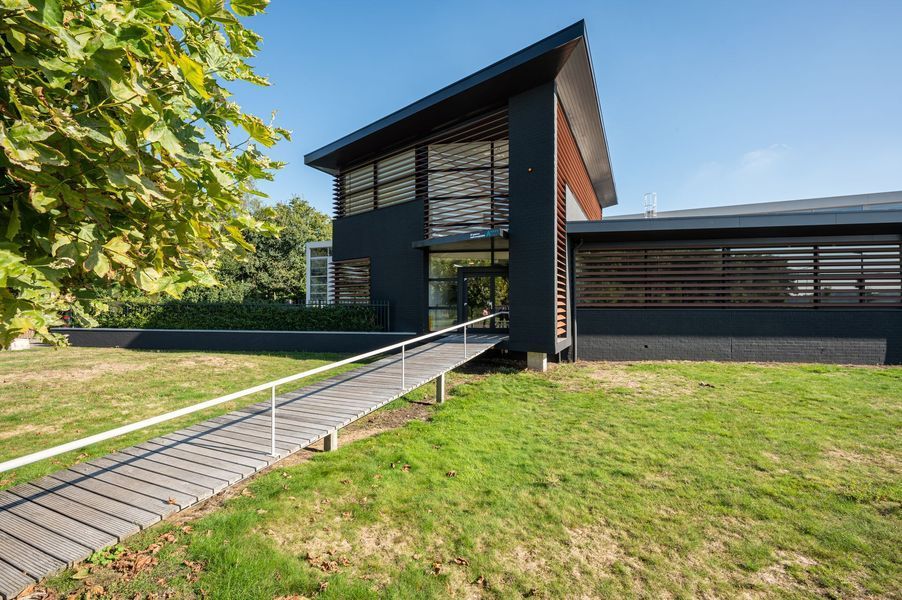Moderne zwarte woning met hellingbaan en grote ramen, gelegen op een grasveld.