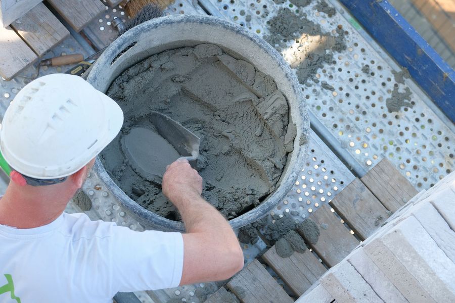 Een arbeider met een veiligheidshelm mengt nat cement in een grote ronde container op een bouwterrein.