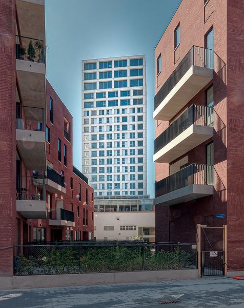 Een stedelijke binnenplaats tussen appartementencomplexen van rode baksteen, met op de achtergrond een hoge witte wolkenkrabber.