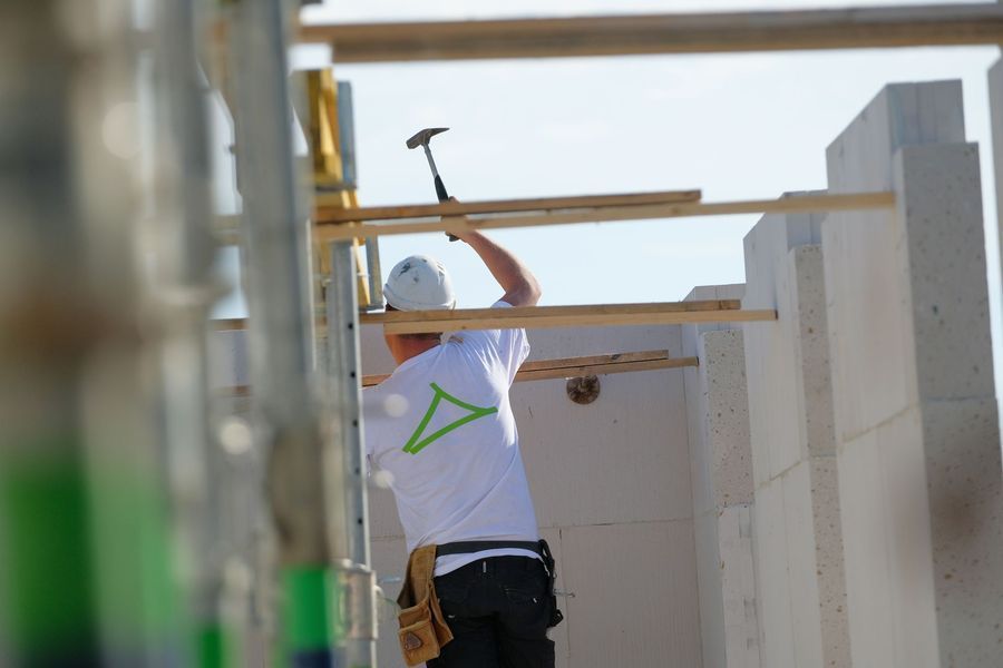 Een bouwvakker hamert een balk vast aan een gebouwframe in aanbouw.