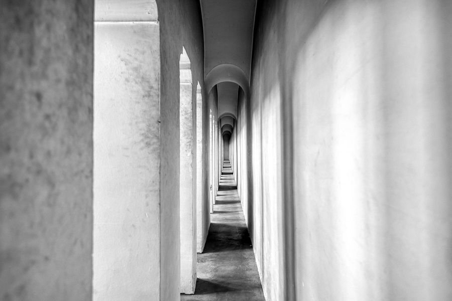 Lange, smalle betonnen corridor met herhalende bogen en een verdwijnpunt.