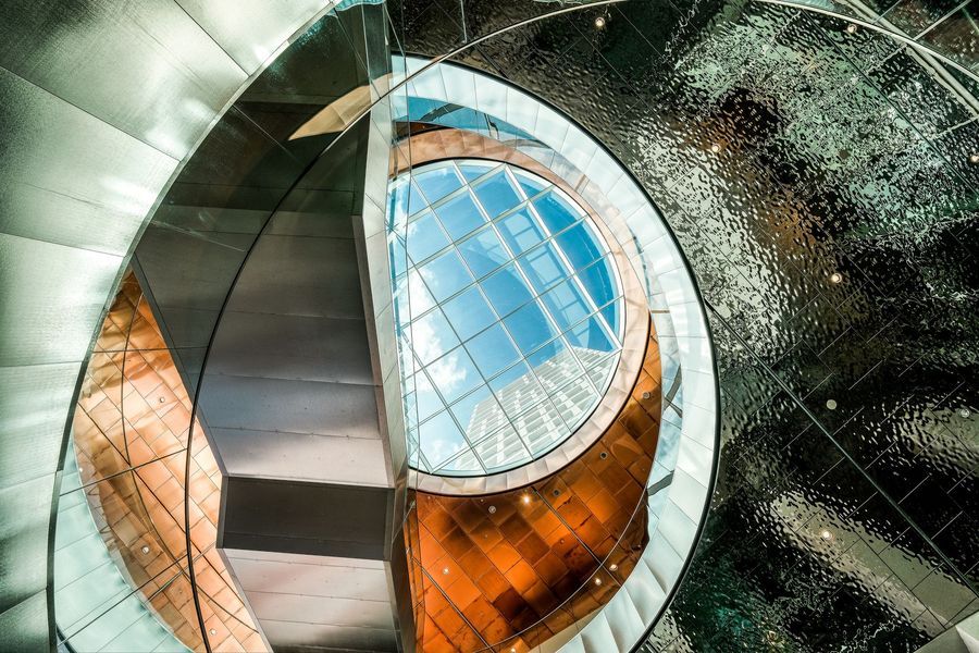 Abstracte wenteltrap met glazen dakraam, metalen rondingen en oranje accenten.