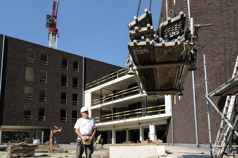Bouwplaats met een hangend betonnen platform en een arbeider met een helm die eronder staat.