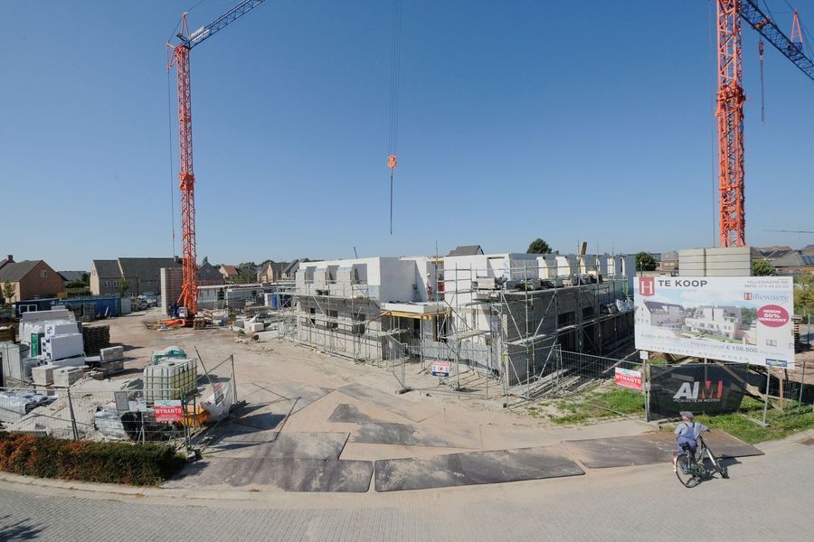 Bouwplaats met kranen, steigers en een gedeeltelijk gebouwd gebouw onder een heldere blauwe hemel.