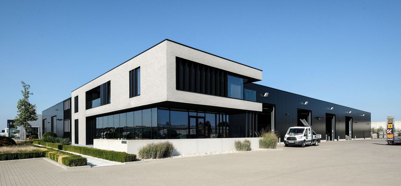Een graafmachine graaft een sleuf naast een bakstenen gebouw op een modderige bouwplaats.