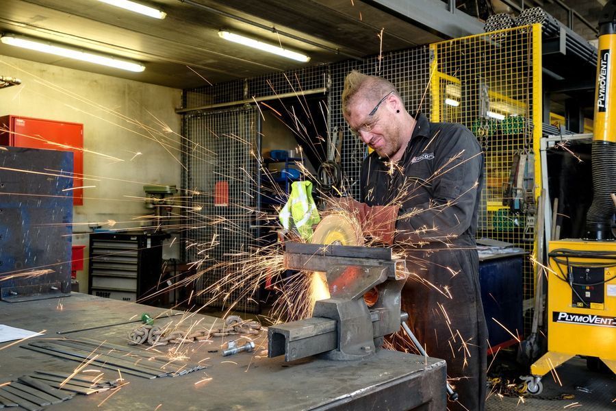 Een arbeider gebruikt een slijpmachine, waardoor er vonken over de werkplaatsvloer vliegen.