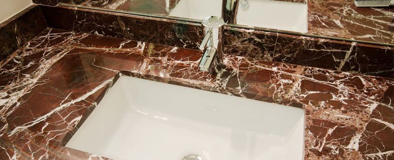 Un lavabo de baño con encimera de mármol rojo y un espejo.