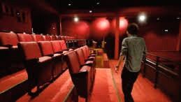 Un hombre camina por un teatro vacío con asientos rojos.