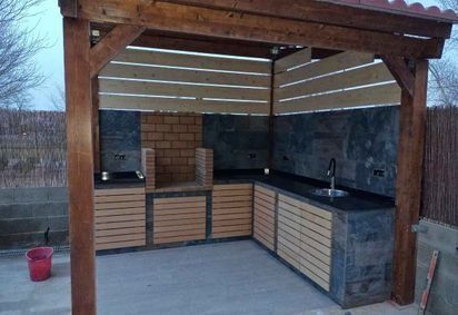 Un cenador de madera con un horno de ladrillo y un fregadero debajo.