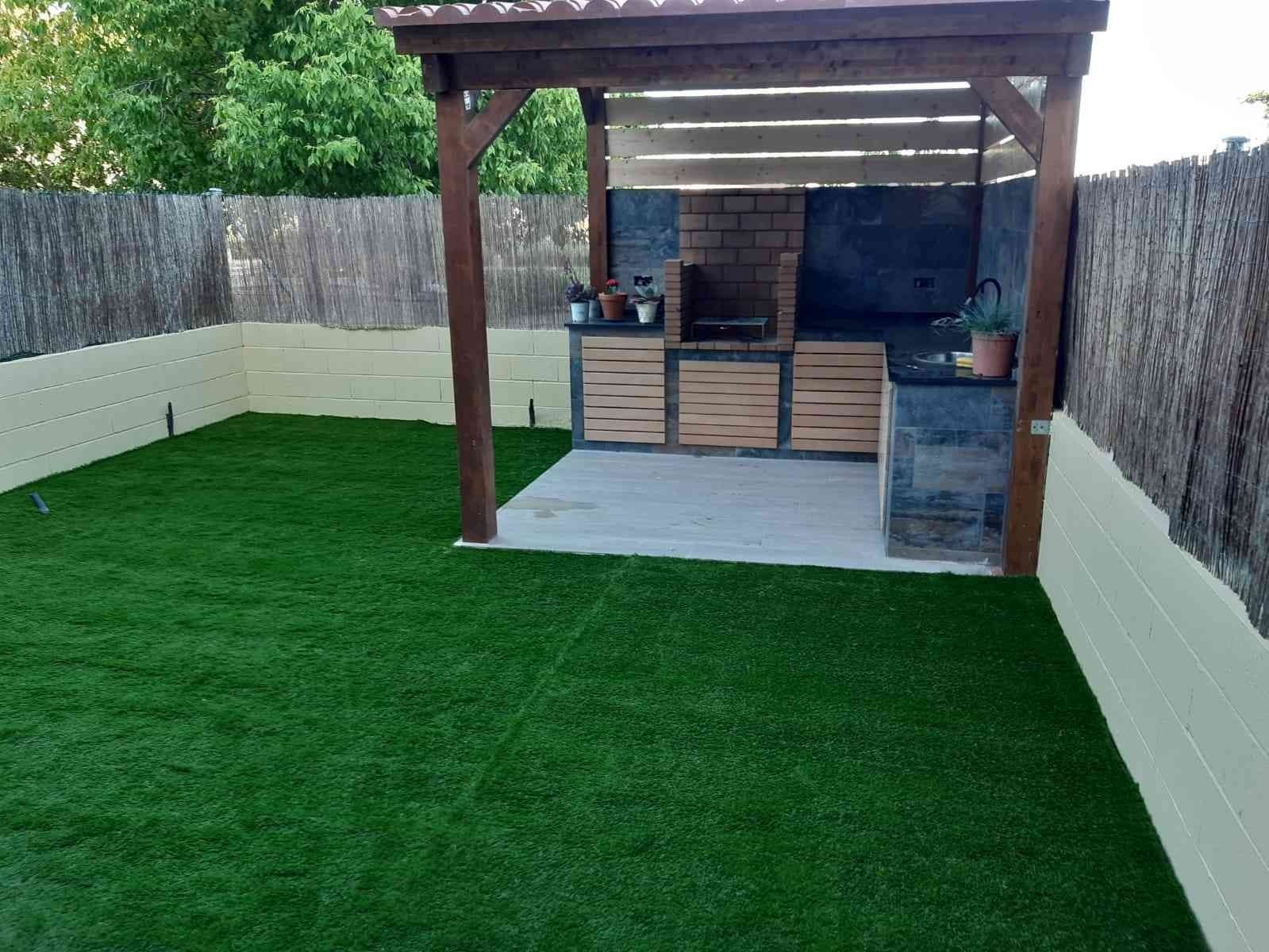 Un patio trasero con un cenador de madera y una parrilla.