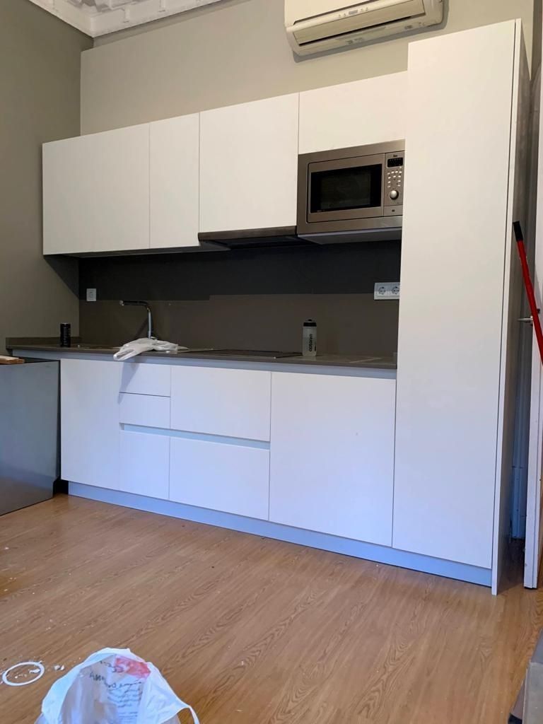 Una cocina con gabinetes blancos, un microondas y un fregadero.