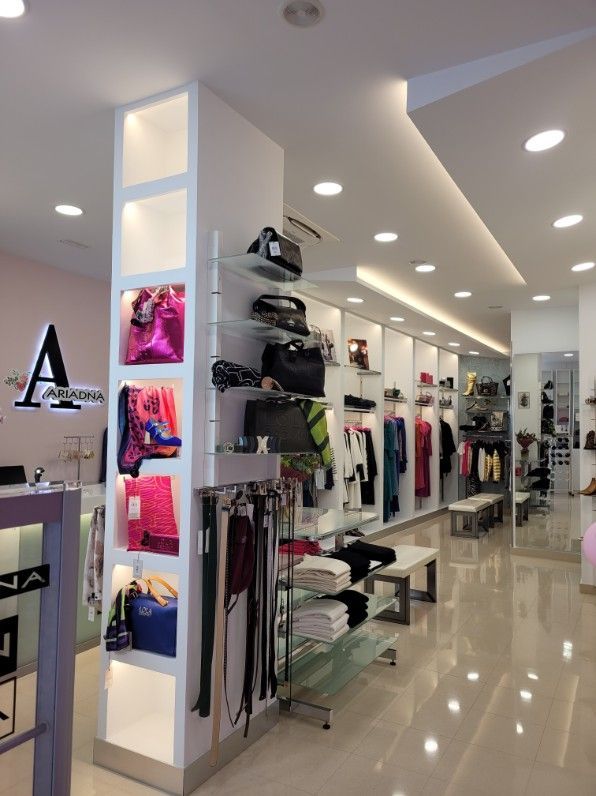 Interior de una boutique de moda con paredes blancas, estantes de exhibición y mercadería, incluidos bolsos y ropa.