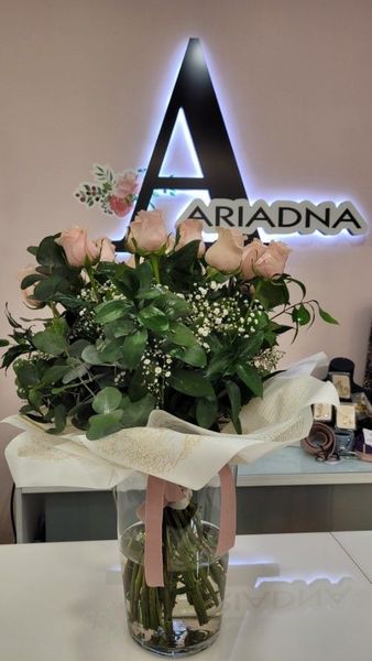 Ramo de rosas rosadas y vegetación en jarrón de cristal, delante de un cartel que dice 
