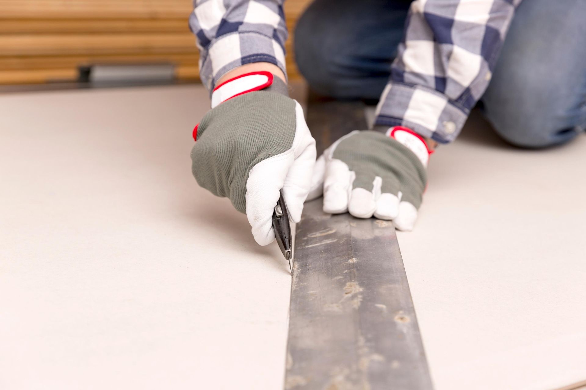 Person, die mit Handschuhen Trockenbauwände mit einem Universalmesser schneidet.