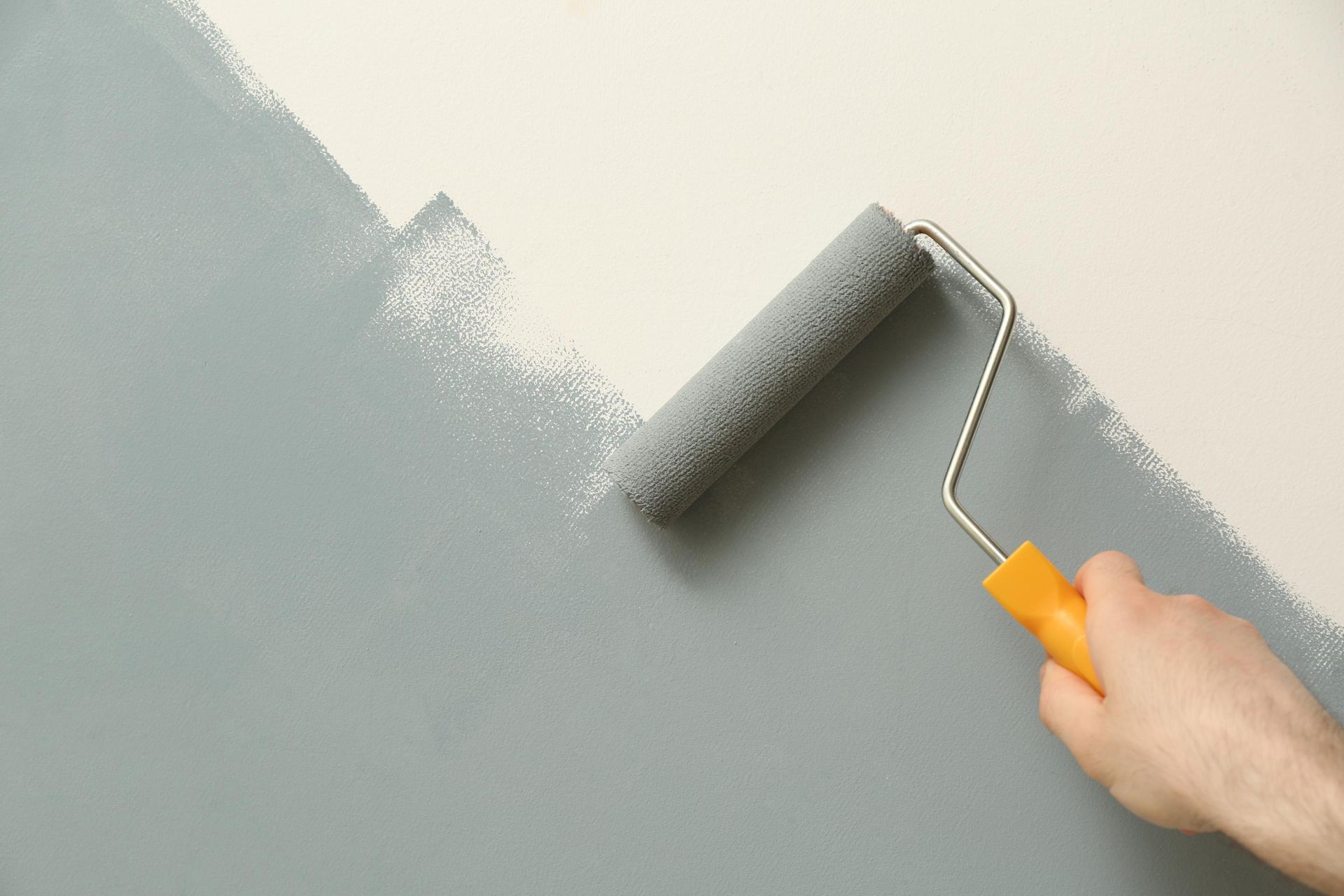 Person, die eine Wand mit einer grauen Farbrolle streicht und die weiße Oberfläche mit grauer Farbe bedeckt.