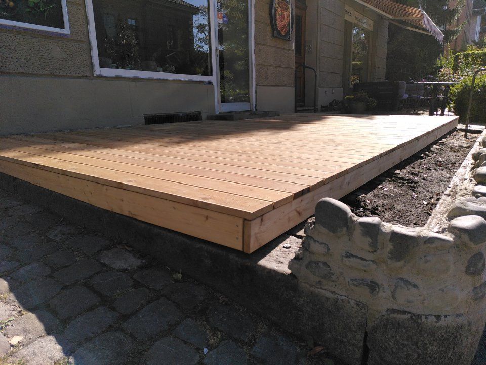 Eine hölzerne Rampe neben einem Haus, die sich über eine steinerne Terrasse im Freien erstreckt.