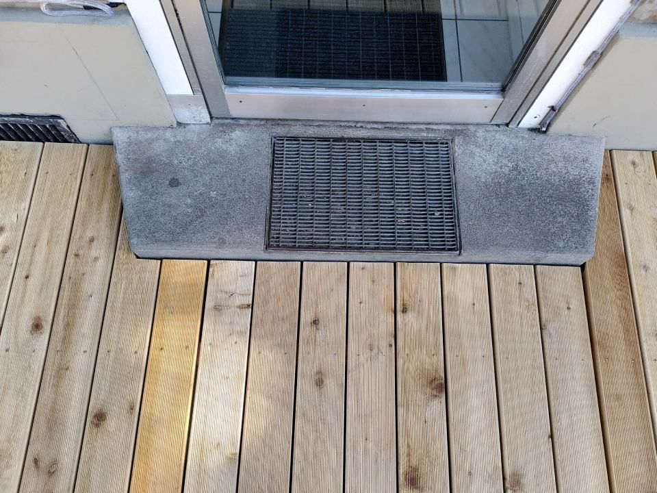 Betonfussmatte vor einer Glastür auf einer Holzterrasse