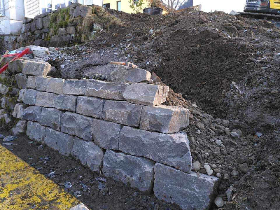Steinstützmauer neben einem Erdhang mit gelb gestrichenem Bordstein im Vordergrund
