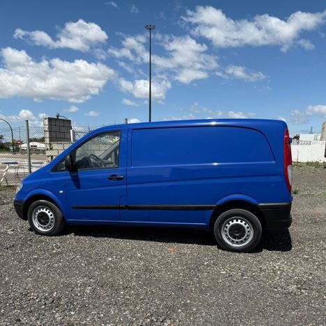 Furgoneta de carga azul estacionada sobre grava bajo un cielo parcialmente nublado.