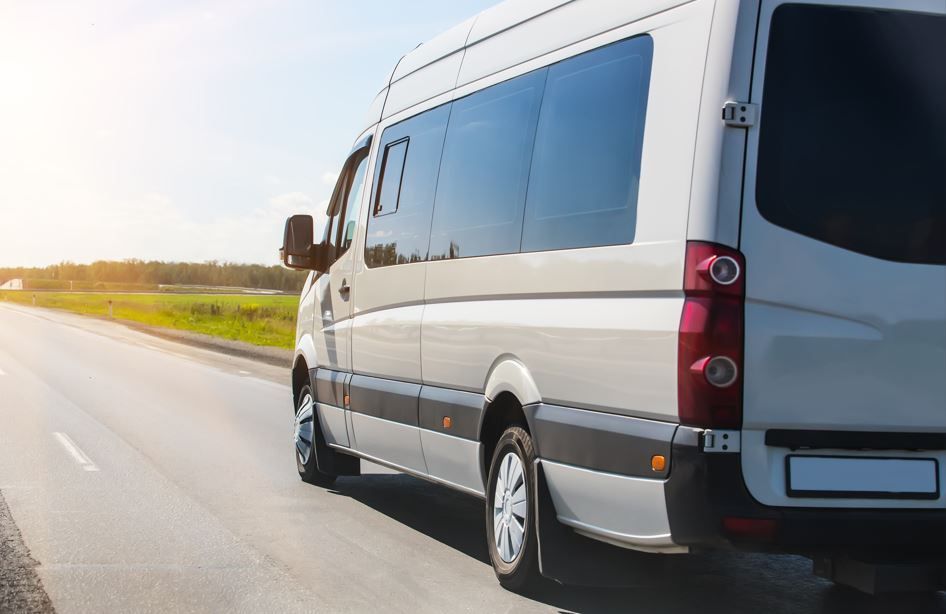 Furgoneta de pasajeros blanca circulando por una carretera asfaltada, día soleado.