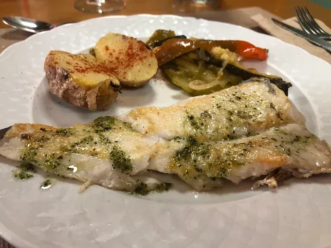 Un plato blanco cubierto con pescado y patatas sobre una mesa.