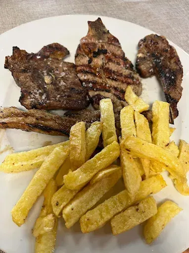 Un plato blanco cubierto con carne y papas fritas.