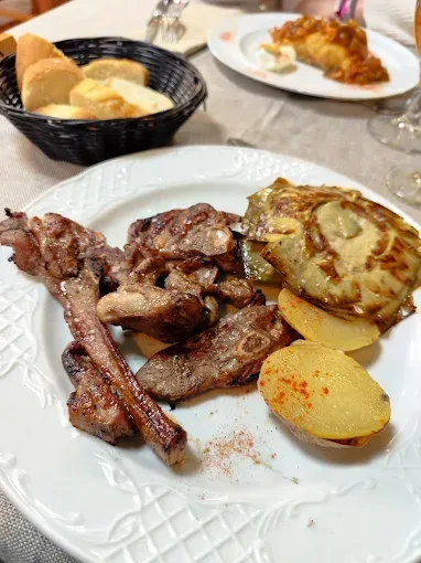 Un plato blanco cubierto con carne y patatas sobre una mesa.