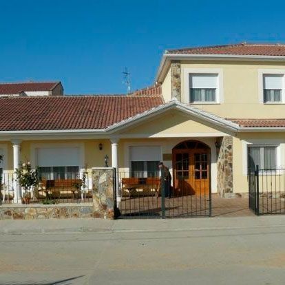 Un hombre está parado frente a una casa amarilla con un techo de tejas rojas.