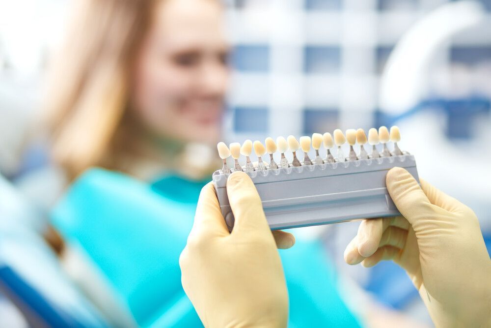 Un dentista sostiene una tabla de colores de dientes frente a un paciente.