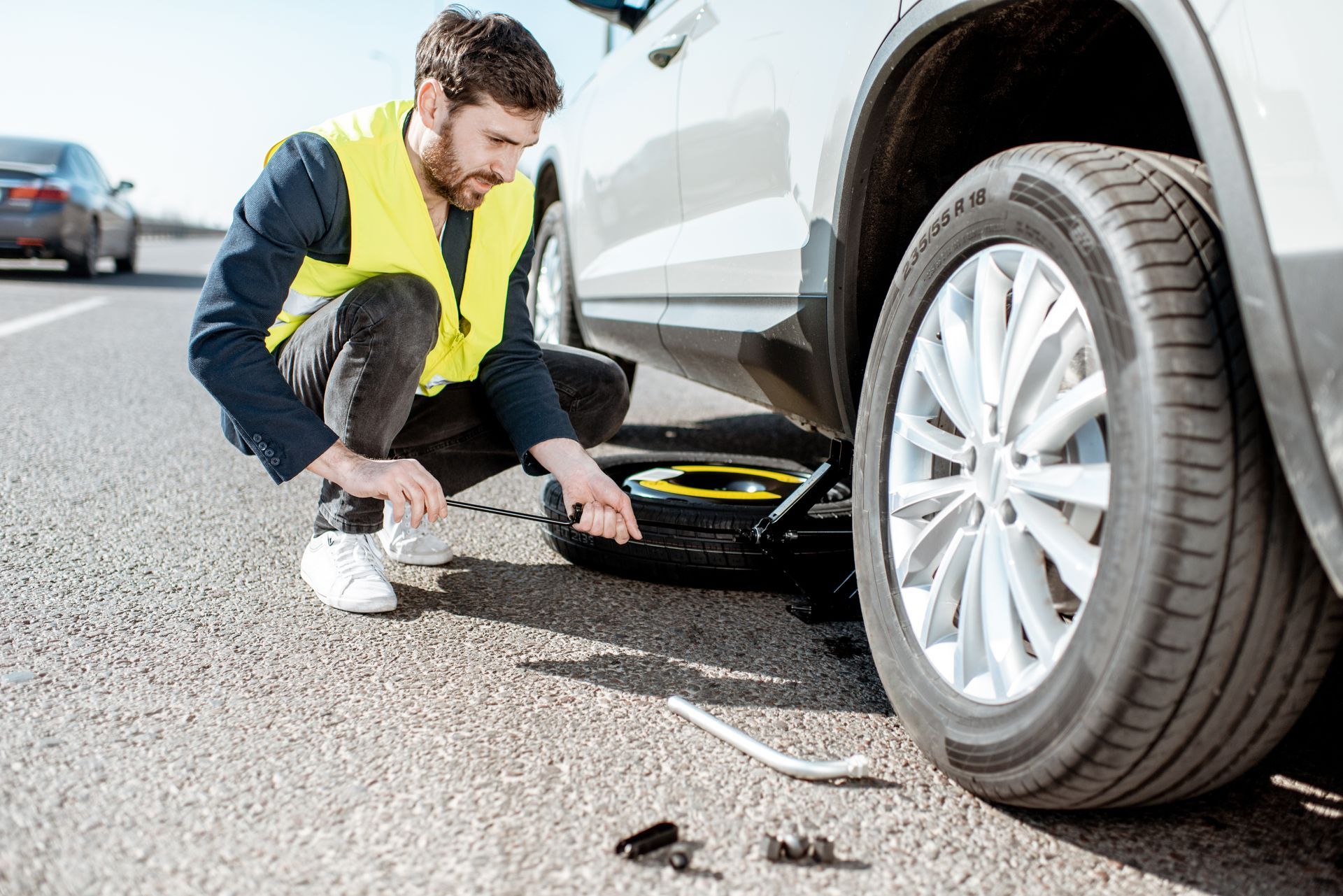 Un homme en gilet jaune change une roue sur le bas-côté.