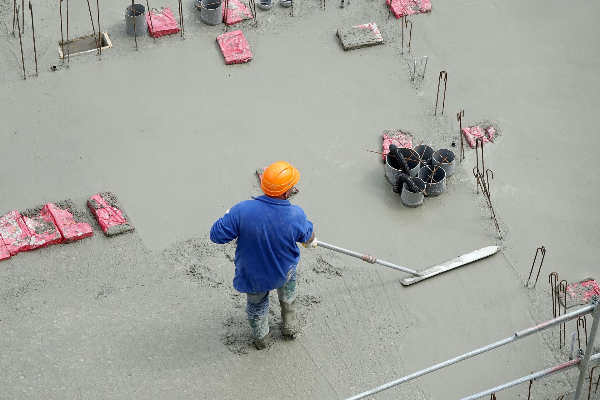 Individu en bleu de travail lissant du béton sur un sol de chantier