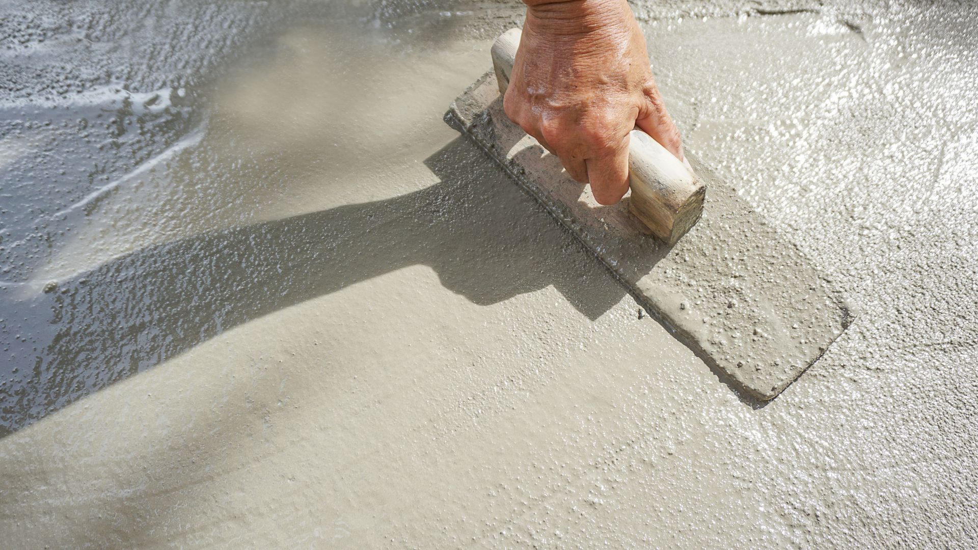 Individu passant une truelle pour lisser une chape de béton