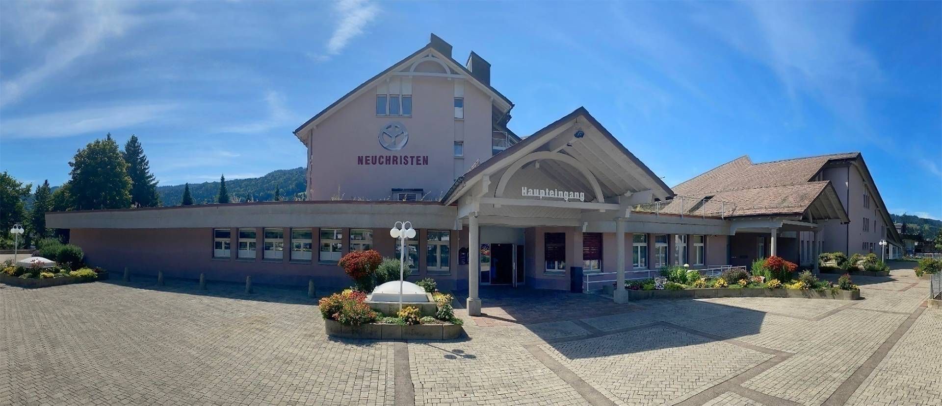 Ein hellrosa Gebäude mit Giebeldach, unter blauem Himmel und auf Kopfsteinpflaster.