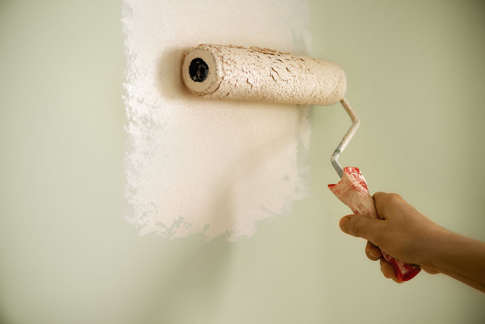 Peinture à la main d'un mur clair au rouleau ; une tache de peinture blanche est visible.